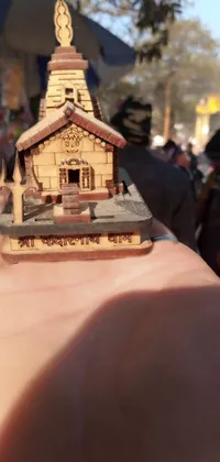 Looking for a beautiful live wallpaper for your phone? Look no further! This stunning wallpaper features a miniature model of a church held in a person's hand, set against the backdrop of an old Japanese street market