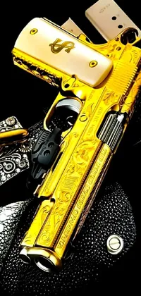 This phone live wallpaper features a stunning golden gun resting on a black surface with detailed and vibrant designs engraved on the barrel and handle