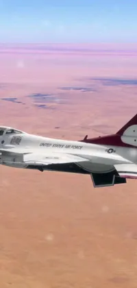 This live wallpaper showcases an impressive display of a fighter jet soaring over a vast desert plain in maroon and white colors, representing the United States Air Force