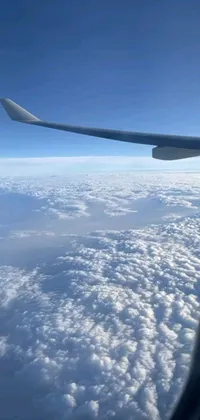 This phone live wallpaper features an awe-inspiring image of an airplane wing soaring above a sea of fluffy white clouds