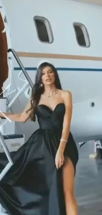 The phone live wallpaper showcases a woman wearing a black strapless dress standing in front of a private jet