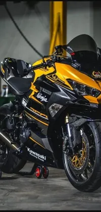 Looking for an edgy live wallpaper that captures the thrill of motorcycle racing? Look no further than this stunning design featuring a black and yellow ninja-inspired bike parked inside a dark garage
