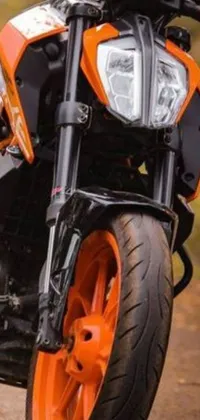 This live phone wallpaper showcases a black and orange motorcycle with ribbed tires on a dirt road