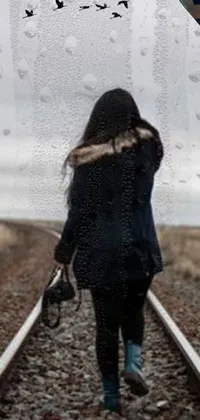 This phone live wallpaper features a solemn woman walking along a rain-soaked train track