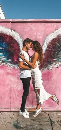 This live wallpaper features a romantic couple kissing in front of a vibrant pink wall adorned with angel wings