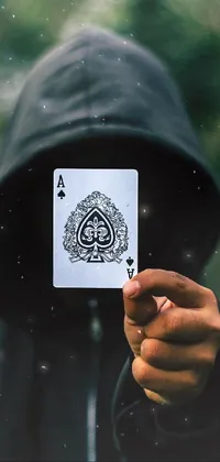 This phone live wallpaper features an intriguing image of a person holding a playing card in front of their face, dressed in a black hoodie and jeans, exuding a mysterious and edgy vibe