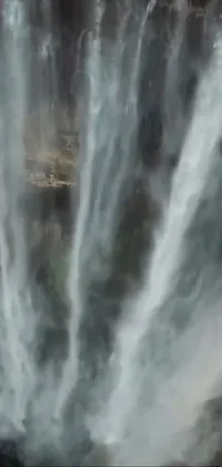 This phone live wallpaper is a breathtaking natural scene of a group of people standing in front of a mesmerizing waterfall