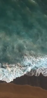 This phone live wallpaper features an incredible aerial image of a surfer on a black sand beach
