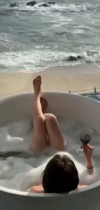 This stunning live wallpaper depicts a person lounging in a bathtub by the ocean