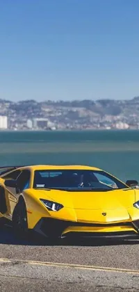 This lively phone live wallpaper features a yellow Lamborghini Aventador sports car driving down a picturesque road alongside a body of water