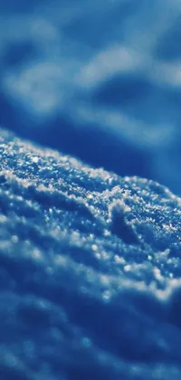 This blue-themed phone live wallpaper showcases a close-up macro photograph of a snowy surface by Alexander Bogen