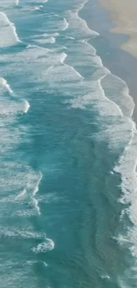 Looking for a mesmerizing live wallpaper for your phone? Look no further than this stunning image of a large body of water next to a sandy beach
