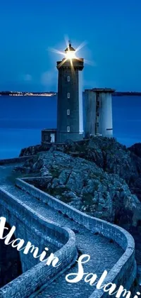 This live wallpaper showcases a breathtaking nighttime scene featuring a majestic lighthouse situated on top of a rocky outcrop above the ocean