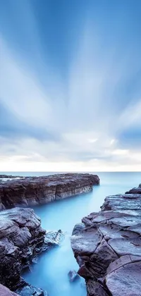 This phone live wallpaper features a serene body of water set against a rocky beach