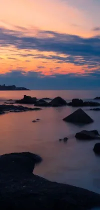 This phone live wallpaper showcases a serene sunset over a serene body of water, with rocks in the foreground