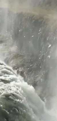 This phone live wallpaper depicts a daring surfer riding on top of a majestic waterfall