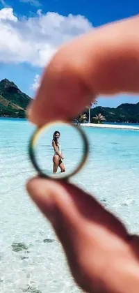 This breathtaking live phone wallpaper features a captivating scene of a ring held in front of crystal clear water against the backdrop of a stunning ocean
