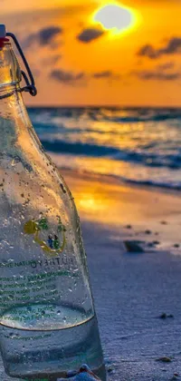 This stunning phone live wallpaper depicts a bottle resting on a sandy beach as the sun sets on the emerald coast