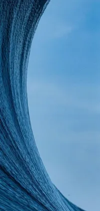 This phone live wallpaper portrays a digital art of a surfer riding a massive wave on his surfboard against a winter blue drapery background
