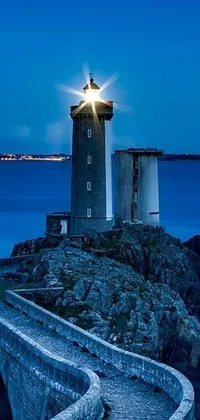 This phone live wallpaper showcases a stunning photograph of a lighthouse on a rocky outcropping by the ocean at nighttime