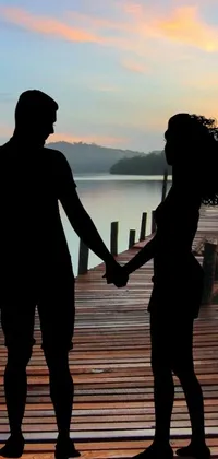 This phone live wallpaper features a couple holding hands on a dock at sunset, overlooking a serene lake with a wooden dock in the foreground