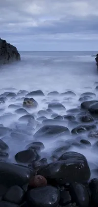 This phone live wallpaper features weathered rocks on a beach overlooking dark, churning water