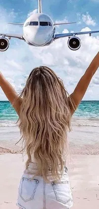 This live phone wallpaper depicts a blond woman standing on a beach with her arms raised to the sky, along with an airplane flying overhead