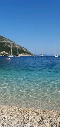 Enjoy a stunning live wallpaper featuring a group of boats floating atop crystal clear blue waters against a mesmerizing Mediterranean beach backdrop