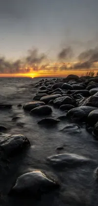 This live wallpaper showcases a serene beach scene with rocks and a magical sunset