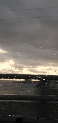 This phone live wallpaper depicts a breathtaking view of a water body under a cloudy sky seen through the car's window