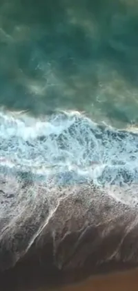 This live phone wallpaper features an exciting aerial shot of a surfer riding a wave on a sandy beach