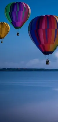 This colorful live wallpaper displays a group of hot air balloons flying over a peaceful body of water