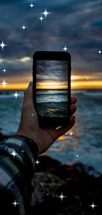 This phone live wallpaper features a stunning image of a picturesque ocean sunset captured through a phone's screen as someone photographs the scene