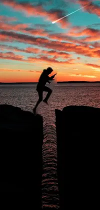 This phone live wallpaper shows a daring leap into the sea from a cliff silhouette against a stunning sunset in Boston