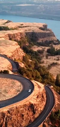 This stunning live wallpaper features a car driving down a winding road alongside a beautiful body of water on a cliff in Oregon
