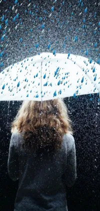 This live phone wallpaper depicts the silhouette of a woman standing under a deep blue sky as a torrential downpour of rain falls about her