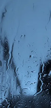 This stunning live wallpaper for your phone features a close up of a rain-soaked window, with shades of blue and grey creating a calming and serene vibe