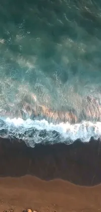 This phone live wallpaper depicts a surfer riding a wave on a sandy beach covered in black sand