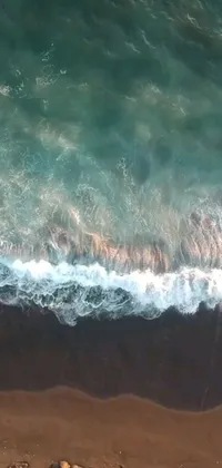 Enjoy the ultimate summer vibes on your phone with this breathtaking live wallpaper! AGuaranteed to give you a sense of adventure, this aerial shot from a drone showcases a skilled surfer riding the waves atop the sandy beach as the ocean winds carry your troubles away