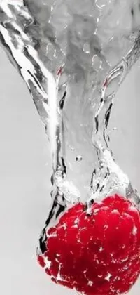 This lively phone wallpaper showcases a juicy raspberry dropping into a glass of water, creating colorful ripples throughout