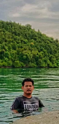 This phone live wallpaper showcases a man in a tropical body of water surrounded by lush trees and the vast sea in the background
