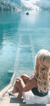 This phone live wallpaper features a luxurious scene in which a woman is sitting on a dock beside a body of water while relaxing and scrolling through her phone
