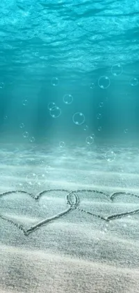 This phone live wallpaper features two hearts drawn in the sand under the water