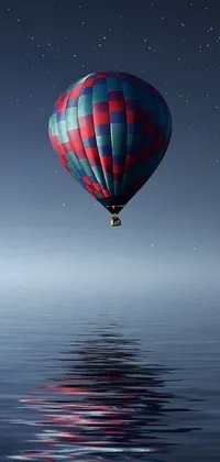 This phone live wallpaper depicts a hot air balloon flying over a calm body of water at night