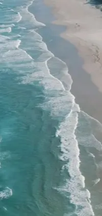 Decorate your phone with a mesmerizing live wallpaper that showcases a large body of water splashing on a sandy beach