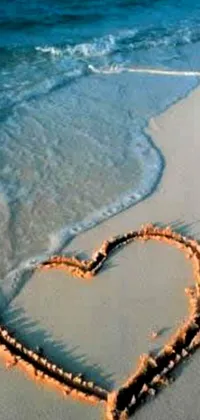 This mobile live wallpaper showcases a heart design etched on the sand at a beautiful beach location