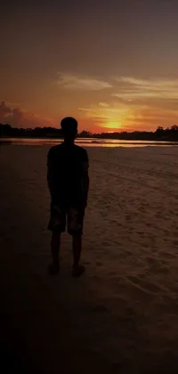 This phone live wallpaper showcases a mesmerizing scene of a person standing on a sandy beach, surrounded by warm colors of the sunset