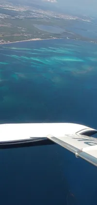 This phone live wallpaper features the realistic wing of an airplane flying over a colorful body of water with coral reefs and palm trees in the background