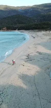 This phone live wallpaper features two people cycling on a sandy beach against clear blue skies and rolling waves