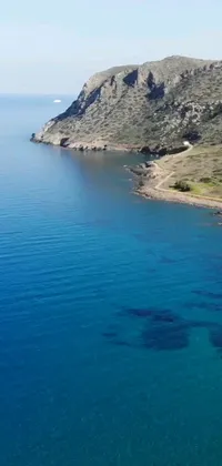 This stunning live wallpaper depicts a serene view of a vast body of water next to a lush green hillside in the Costa Blanca region